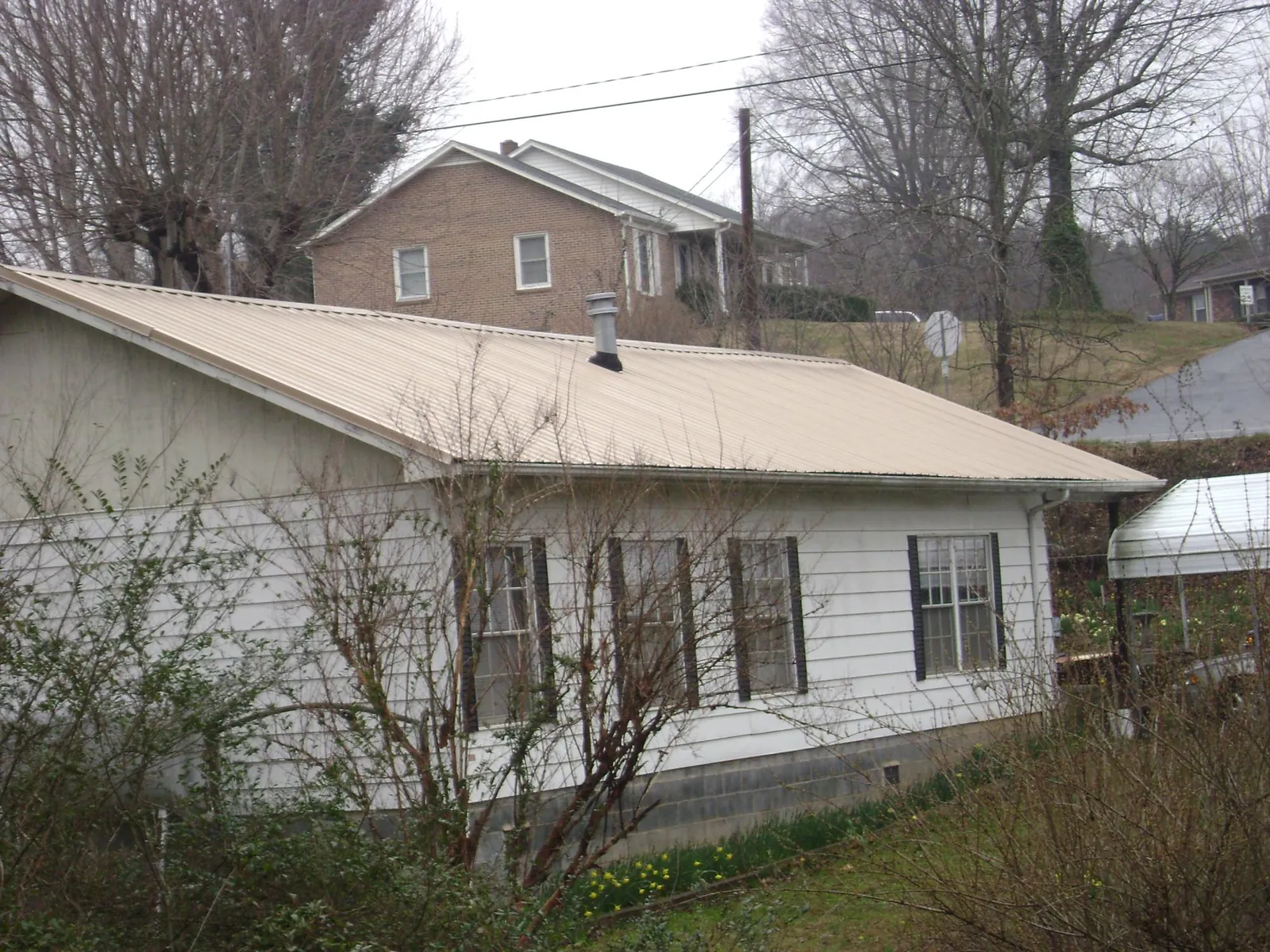 Tan metal roof on a white sided house set into a hillside — Commercial Roofing by Roofing Brothers in Greenwood